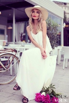 Biała maksi sukienka z kapeluszem. Obok kwiaty i rower, całość prezentuje się bardzo dziewczęco  ...