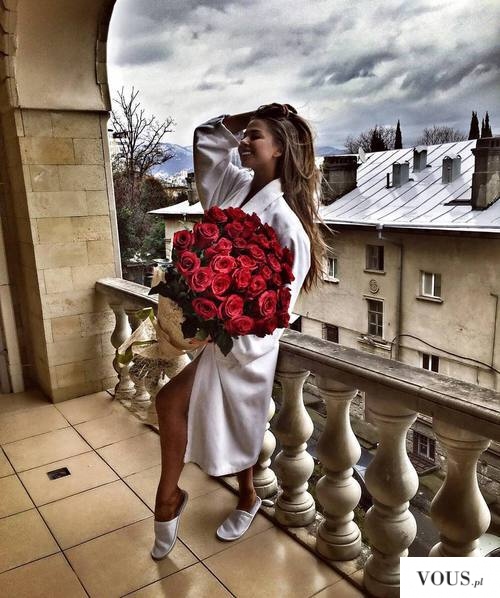 Kobieta z bukietem róż w białym szlafroku na balkonie