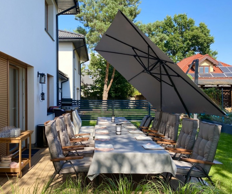 Rozkładany parasol ogrodowy ustawiony nad długim stołem jadalnym w ogrodzie. Dzięki dużej czaszy ...