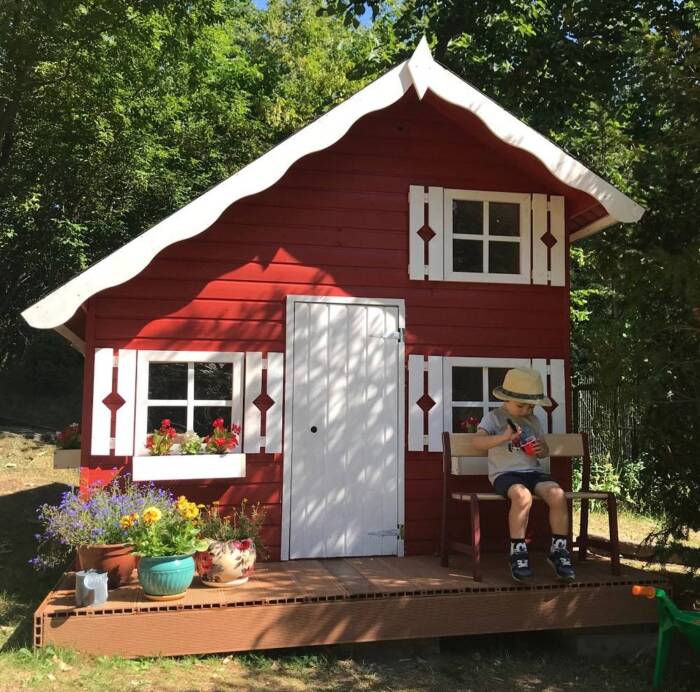 Drewniany domek ze spadzistym dachem i małym pięterkiem pomalowany na czerwono z białymi okienni ...